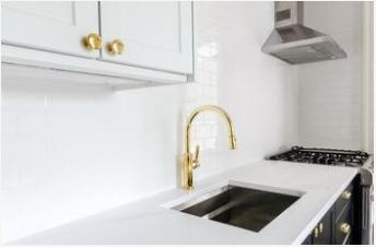Kitchen with white backsplash, gold faucet, and gold cabinet knob